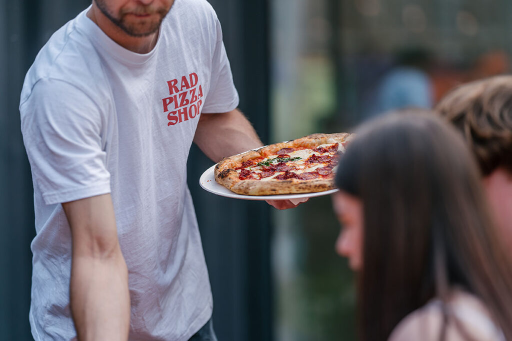 A Rad Pizza Shop staff member serving a pizza