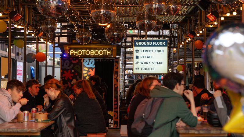 The entrance area of Spark York full of people on benches eating food from traders, with a Photobooth in the distance