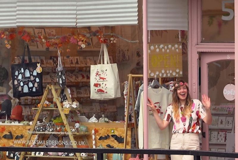 A woman smiling outside a shop called "Just Smile Designs"