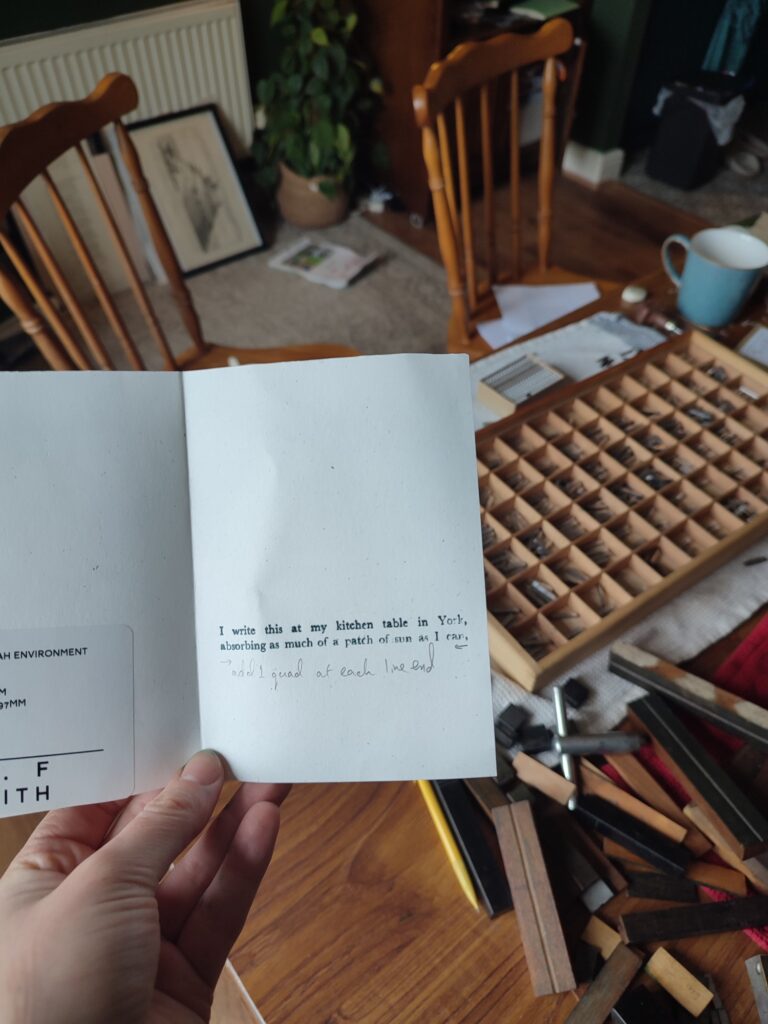 A piece of paper saying "I write this at my kitchen table in York, absorbing as much of a patch of sun as I can"